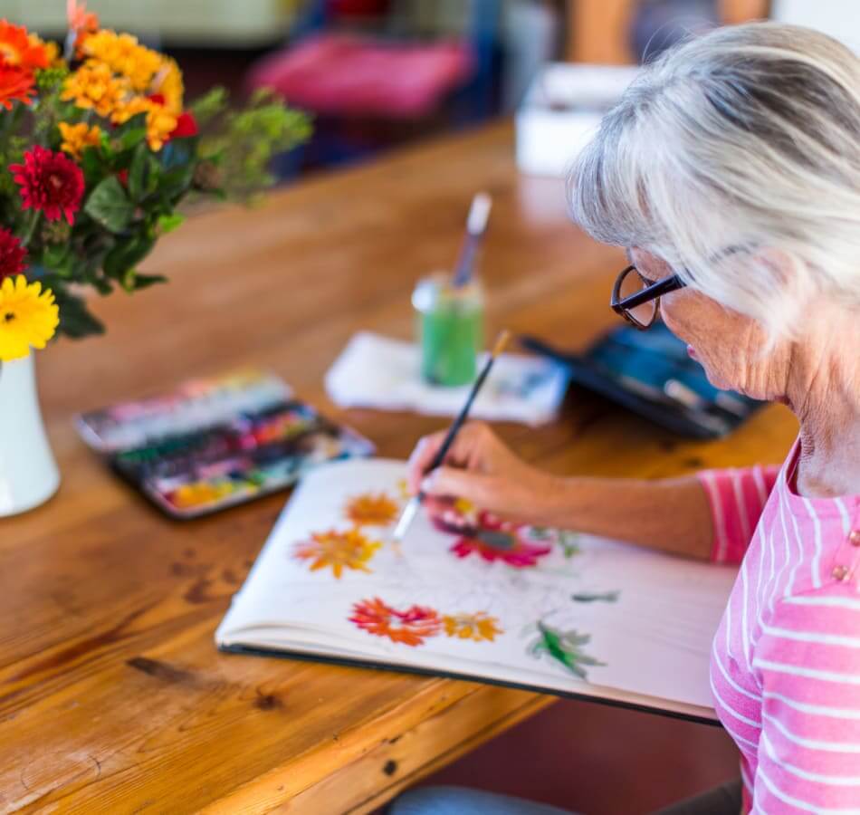 Senior woman painting colorful flowers during a creative activity at The Village of Meyerland.